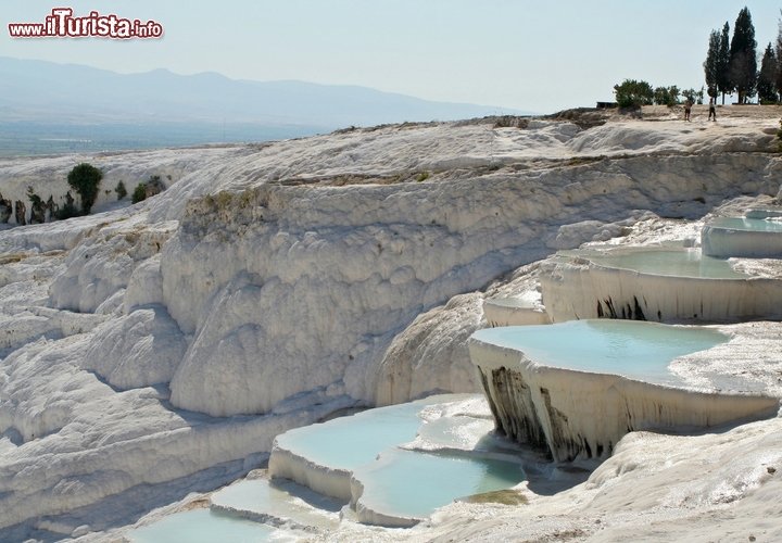 Cascate Pamukkale, Denizli, Turchia - Nella Turchia sud-occidentale, nei pressi di Denizli, si sviluppano delle cascate uniche. Il nome Pamukkale, che significa “castello di cotone”, la dice lunga su un sito naturale che assomiglia a un’architettura perfetta, simile a una candida fortezza o a una cascata gelata. Sono come delle Cascate Pietrificate, in realtà delle fonti termali emerse in seguito ai movimenti tettonici, che oggi sgorgano dalla montagna e la colorano di bianco ricoprendola di gesso e calcare. Tra un getto e l’altro si formano delle vere e proprie piscine naturali, che digradano verso valle come terrazzamenti d’acqua e sono pronte ad accogliere e ristorare i turisti. La primavera e l’estate sono i momenti ideali per sguazzare tra una pozza e l’altra, ammirare le conformazioni calcaree e dirigersi all’antica città di Hierapolis, che insieme alle cascate di Pamukkale è uno dei siti Patrimonio dell’Umanità dell’UNESCO.