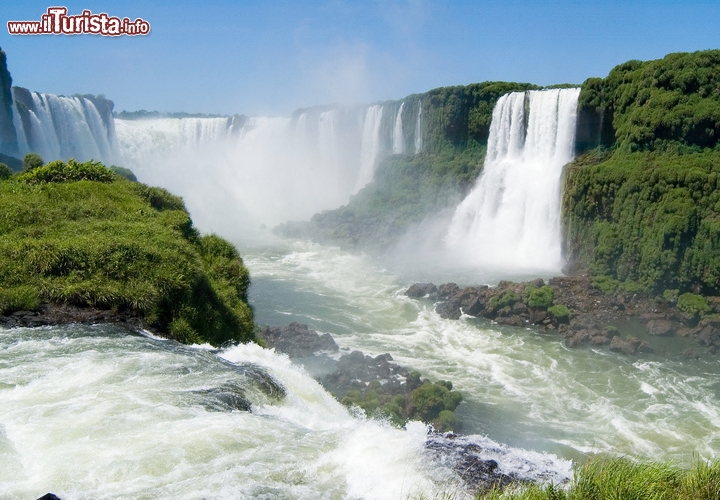 Cascate Iguazù, Puerto Iguazú, Argentina/Foz do Iguaçu, Brasile - Le cascate Iguazù sono altrettanto famose di quelle del Niagara ma ancor più spettacolari, per il fronte di 2,7 km, incastonate tra Argentina e Brasile con tutta la potenza dei loro 275 getti, con un salto massimo di 84 metri.. Secondo la leggenda sarebbero nate dalla furia di un dio, innamorato di una mortale e non corrisposto. Doveva essersi arrabbiato parecchio, per dar vita a un sistema così grandioso di cascate colossali e cascatelle, ma per noi è stata una fortuna: il rombo dell’acqua, il vapore che sale e la vegetazione lussureggiante sono il contorno di veri e propri giganti, prima fra tutte la Garganta del Diablo (Gola del Diavolo), una cascata lunga 700 metri, ed alta 50, composta da 14 getti d’acqua. Tutt’intorno, tra le minuscole gocce d’acqua sospese in aria, vibrano i colori dell’arcobaleno, circondati da una vegetazione lussureggiante, e le ali leggere di centinaia di farfalle.