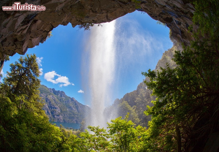 Cascata del Saltillo, Parco Nazionale Lanin, Argentina - Ci trovaimo nella zona di San Martin de los Andes, in Patagonia e qui oltre il vulcano, che da al nome al parco, merita una visita la bella cascata de el Saltillo, una delle più fotogeniche del sudamerica. Il vantaggio fotografico di questa caduta è il grande spazio alle spalle del getto d'acqua, che consente una prospettiva diversa dal solito, potendo fotografare, praticamente, da dentro una specie di grotta. Il salto è complessivamente di 20 metri, quindi abbastanza modesto, ma immerso in una cornice naturale fantastica, con abbondante vegetazione. Sullo sfondo si notano infatti le acque del lago Huechulafquen, e ci troviamo in una delle zone più piovose della Patagonia argentina - © Dmitry Saparov / Shutterstock.com