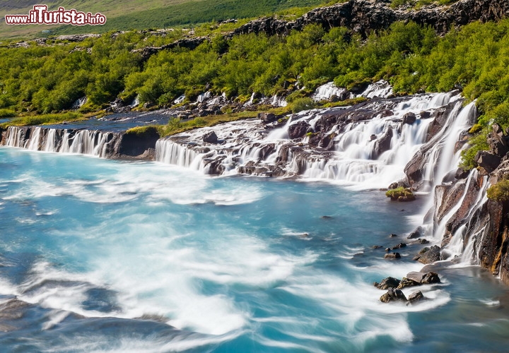 Hraunfossar, le spettacolari cascate nell'Islanda occidentale - Non è tanto il loro salto ad impressionare, quanto la magia del paesaggio nel suo insieme. La traduzione dall'islandese di Hraunfossar significa le "Cascate di Lava", e in effetti le acque che si gettano nel fiume Hvítá scaturiscono quasi magicamente dall'interno di una antica colata di lava, con un fronte complessivo di oltre 900 metri. Le acque derivamo da un vicino ghiacciaio chiamato Langjökul, e partendo da esso scorrono nel sottosuolo, per circa 1 km, prima di erompere in superficie e tuffarsi nel fiume.  Di solito la visita di queste cascate include una breve passeggiata alle Barnafoss, le cascate dei bambini, chiamate così per la tragica scomparsa di due bambini caduti nelle acque del fiume. Le Hraunfossar si trovano a Húsafell, non distanti da Reykholt, nel territorio del comune di Borgarbyggð, relativamente vicine alla capitale Reykjavík - © Filip Fuxa / Shutterstock.com