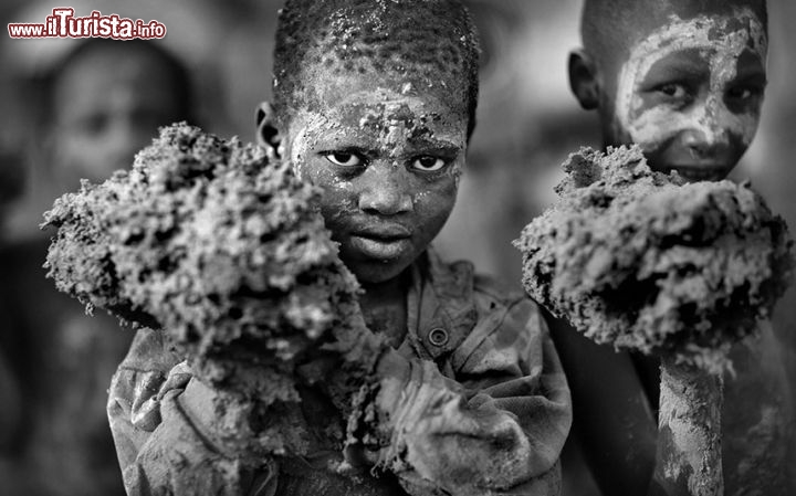 Foto vincitrice del concorso  "Travel Photographer of the Year". Questo scatto raffigura un momento del festival della ricostruzione della moschea di fango a Djenne in Mali. Dopo il monsone estivo la moschea fatta di fango essiccato deve essere restaurata, e tutta la città, compresi i bambini, partecipa alla ricostruzione delle mura color ocra che erano state sciolte delle forti piogge. Il bianco e nero fornisce un elelento di drammaticità ulteriore, come anche la scelta di un diaframma aperto, con poca profondità di campo, che naturalmente concentra l'attenzione sugli occhi del bambino della capitale del Mali - ©  www.tpoty.com - Foto di Timothy Allen 