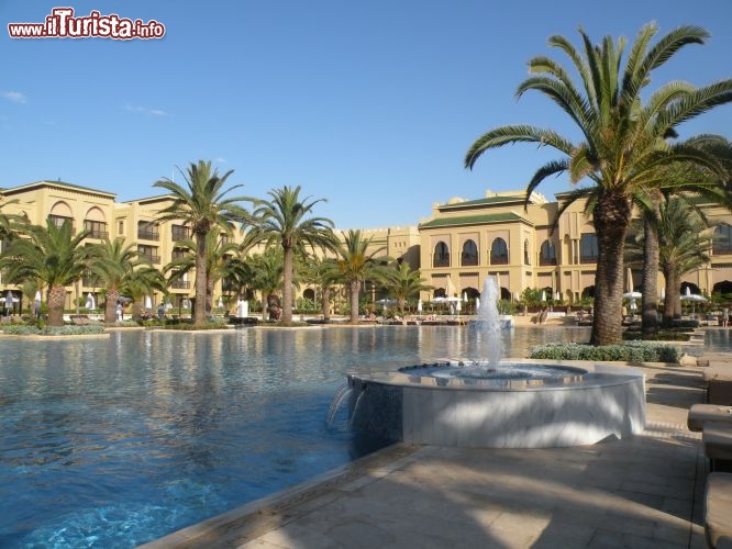 Il sontuoso ingresso del Mazagan Beach & Golf Resort - La visita poi si apre, nell'interno, sulla floreale lobbies dove l’acqua della vivace fontana posta al centro gioca con la luce che filtra attraverso il soffitto di vetro. Le camere e le suite sono disposte a ferro di cavallo, al centro delle quali troviamo la piscina riscaldata a 28 °C ed i giardini interni con palme e coloratissime piante fiorite