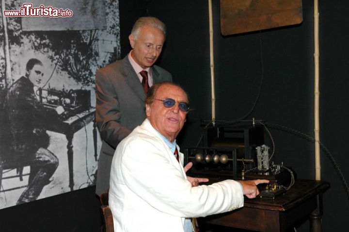 Immagine Renzo Arbore al Museo Pelagalli di Bologna - Il presentatore, nonchè muscista, pugliese ripreso  con il fondatore del museo, Gianni Pelagalli, mentre siede al tavolino trasmettitore delle onde radio, appartenuto a Guglielmo Marconi