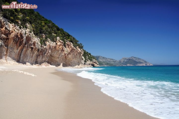 Cala Luna, Sardegna - Ha un nome romantico e seducente Cala Luna, una delle spiagge più belle della Sardegna orientale, situata nel Golfo di Orosei. La sabbia grossa mista a sassi, di un colore chiaro luminosissimo, le conferisce un carattere ruvido e selvaggio, che fa innamorare chiunque abbia voglia di libertà. Per ripararsi dal sole ci sono le ampie grotte che si aprono nelle scogliere vicine: è una meraviglia rifugiarsi al fresco a leggere o mangiare qualcosa, magari mentre i bambini giocano in sicurezza, grazie al fondale basso. La spiaggia è dotata di un punto di ristoro e nei dintorni ci sono molti ristorantini e locali che si animano dopo il tramonto: restate a Cala Luna fino al tramonto, assaporando lunghi bagni nelle sue acque cristalline, e passate la serata vicino al mare. Non ve ne pentirete!
La spiaggia è raggiungibile a piedi mediante un sentiero piuttosto impegnativo che parte da Cala Fuili o da Baunei, oppure via mare con i battelli che partono regolarmente da Cala Gonone o dalla spiaggia della marina di Orosei - © ultimathule / Shutterstock.com