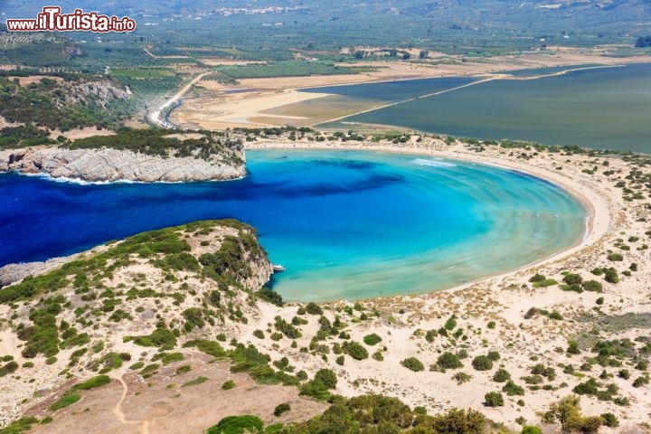 Spiaggia di Voidokilia nel Peloponneso, in Grecia - Nella bella terra ellenica non ci sono solo gli arenili delle sue innumerevoli isole! Anche lungo le coste del Peloponneso troviamo spiagge indimenticabili, come il caso della splendida Voidokilia beach, dalla particolare forma a mezzaluna, che ricorda anche la lettera omega dell'alfabeto greco. La spiaggia, un pò selvaggia e priva di servizi, offre sabbie bianche finissime, mentre un cordone di dune, maculate di macchia mediterranea, separa il mare turchese con la retrostante laguna di Gialova. La spiaggia, che si trova lungo il "dito" più occidentale del Peloponneso, e si affaccia sul mare Ionio, si raggiunge facilmente in automobile da Costa Navarino e da Pylos, e rimane non distante da Kalamata - © Nick Pavlakis / Shutterstock