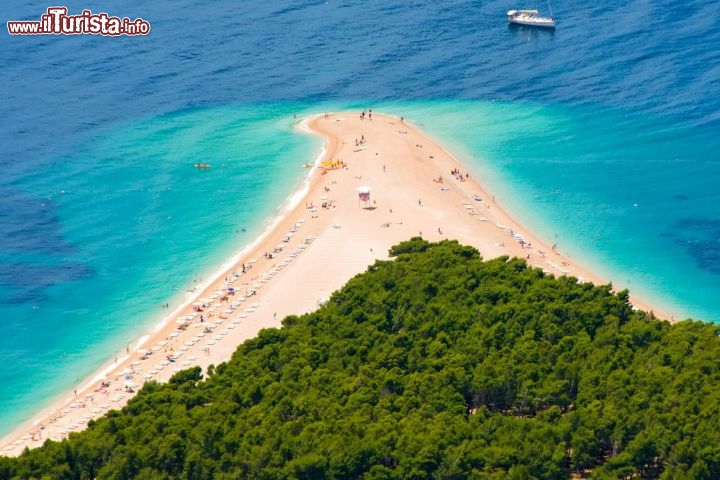 Zlatni Rat sull’isola di Brac, Croazia - La spiaggia di Zlatni Rat, o Corno d’Oro, è un’incantevole lingua di sabbia dorata (una rarità in Croazia) che si allunga su un’acqua caraibica nel sud dell’isola di Brač (Croazia), a 2km circa dal porto di Bol. Si estende nel canale di Hvar, il braccio di mare che separa Hvar da Brač, e per questo è lambita da forti correnti che col tempo l’hanno modellata e le hanno dato la caratteristica forma affusolata. La spiaggia è costituita da ciottoli finissimi, candidi come la neve, che fanno sembrare ancora più brillante l’azzurro del mare, ed è attorniata da colline ricoperte di una pineta freschissima che odora di resina e di Mediterraneo. Essendo la spiaggia più famosa dell’isola (e non è un caso) è generalmente piuttosto affollata, ma è abbastanza ampia da ospitare tutti comodamente, è pulita e ben tenuta, dotata di ogni comfort si possa desiderare: lettini, ombrelloni, punti di ristoro e negozietti di souvenir sono l’allegro contorno di un piccolo paradiso terrestre.
Da Bol è raggiungibile a piedi, attraverso un sentiero che taglia la pineta, con il taxi boat o col trenino, che costa circa 15 kn a persona (sui 2 euro) - © hektoR / Shutterstock.com 