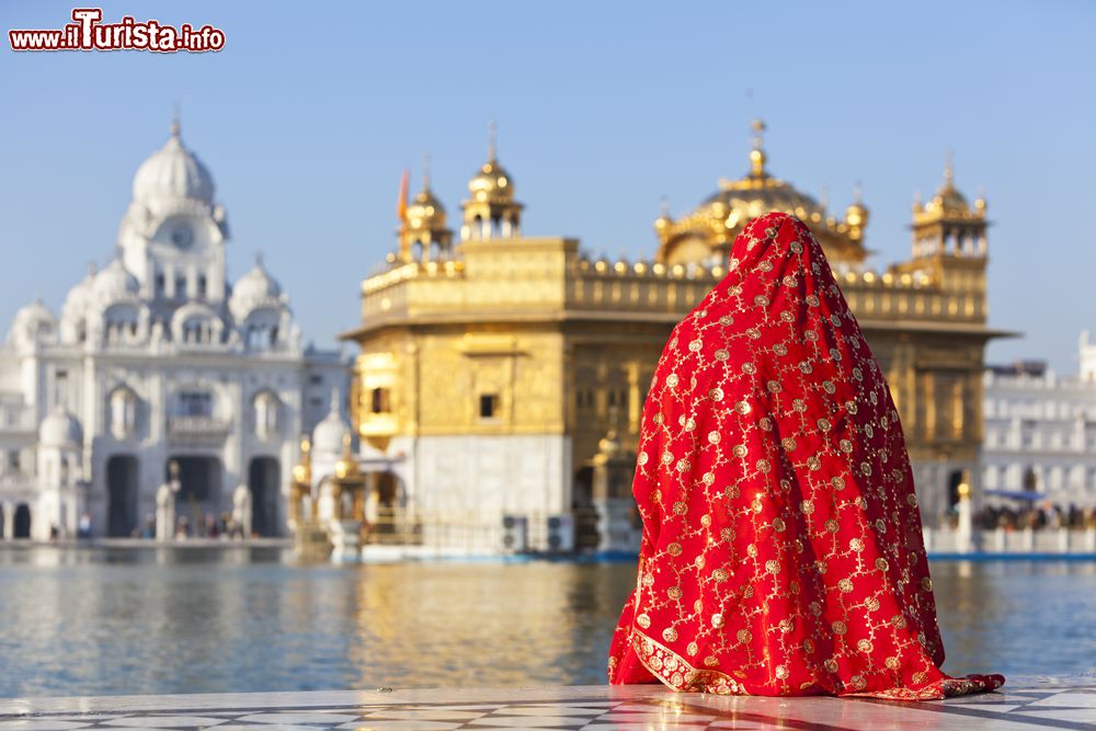 una_donna_con_un_tradizionale_sari_rosso_osserva_il_tempio_doro_a_amritsar_punjab